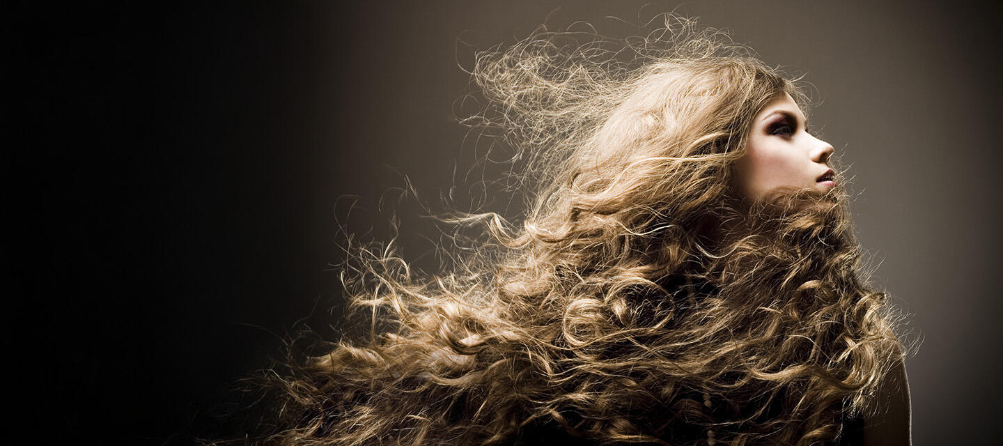 A young blond woman in the spotlight on a dark background, with a gorgeous head of thick, wavy hair 
